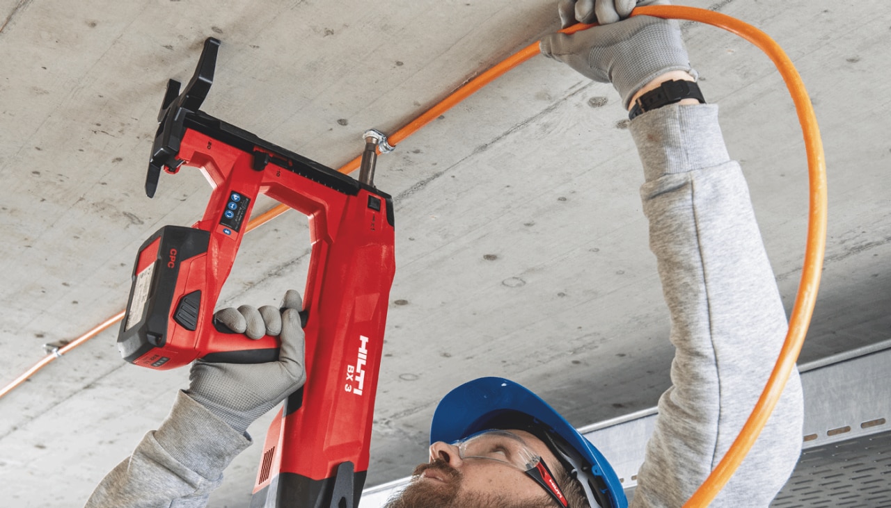 töötaja, kes kasutab hilti tööriista, et pingutada elektrikaableid lae külge.